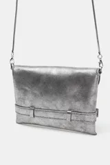 Bolso formato bandolera de material sintético con acabado metálico plateado. Presenta un diseño de solapa frontal con un cinturón decorativo que se cierra con una hebilla metálica en forma de corazón. Incluye un asa bandolera fina de cadena y un bolsillo interior con cierre.