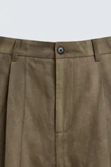 Pantalón de corte relajado confeccionado en mezcla de algodón y lino, con diseño de pliegues frontales, bolsillos laterales y bolsillos traseros de vivo. Presenta cierre frontal con cremallera y botón, con un acabado de lavado especial que le otorga una apariencia única.