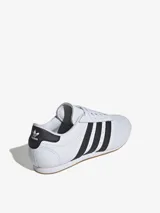 Zapatillas Adidas de cuero blanco con las tres tiras laterales en negro y suela de goma color caramelo.