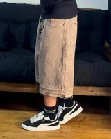 Bermuda de corte baggy color marrón con efecto gastado (lavado vintage), doble carpintero y detalle artesanal visible en el bajo. Incluye un cordón extra confeccionado en la misma tela.