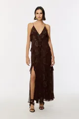 Vestido largo marrón de viscosa con estampado paisley formado por apliques termoadhesivos dorados. Presenta escote en V con tirantes finos, volantes en cascada y una abertura lateral profunda en la falda.