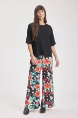 Pantalón palazzo de tela fluida con estampado floral en tonos naranja, celeste y blanco sobre fondo negro.
