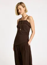 Blusa marrón de punto elástico con corte ajustado, escote recto, tirantes finos, detalle de panel superpuesto en el busto, costura lateral con ligero drapeado, bajo asimétrico con punta lateral larga y pespuntes.