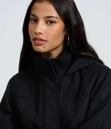 Campera alargada de polivelour color beige, con capucha, cierre frontal con botones a presión y bolsillos con solapa. Presenta un diseño de corte recto y manga larga.