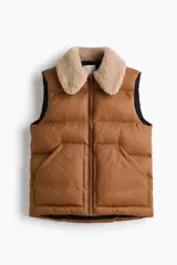 Chaleco acolchado de color tostado con diseño guateado, cuello de sherpa en tono crema, cierre frontal con cremallera y bolsillos frontales tipo parche.