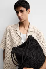 Bolso tipo shopper color crudo, confeccionado en tejido trenzado de algodón con diseño de macramé. Cuenta con dos asas de hombro ajustables que funcionan como cierre del compartimento principal.