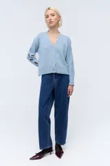 Cárdigan corto celeste de lana con lentejuelas, escote en V, cierre frontal con botones y mangas largas con aberturas.