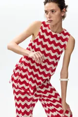 Top sin mangas de punto jacquard estilo crochet con patrón en zigzag de franjas rojas y blancas, cuello redondo y bajo levemente acampanado.