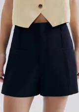 Short de vestir estilo sastrero color azul marino, de tiro alto con bolsillos frontales simulados y costuras verticales decorativas.