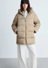 Campera puffer acolchada de color beige, con diseño recto, cuello alto y capucha integrada. Cuenta con cierre frontal de cremallera doble, mangas largas con puños elásticos y dos bolsillos laterales con cierre. Acabado repelente al agua.