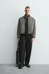 Pantalón negro de corte relaxed fit y estilo wide leg, con pliegues frontales dobles, bolsillos delanteros y detalle de bolsillos traseros de vivo. Cierre frontal cruzado con cremallera y gancho metálico oculto.