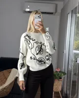 Sweater de tejido de punto con cuello redondo y diseño de bordado lineal en contraste que forma motivos orgánicos y florales. Presenta un corte clásico y mangas largas.