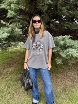 Remera de algodón gris con efecto lavado, de corte holgado y manga corta. Presenta un estampado frontal con diseño de árboles y figuras geométricas a cuadros, acompañado por la frase 'Jardín de Invierno'.