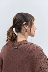 Sweater de punto color celeste, con diseño de trenzas y detalles de cordones entrelazados en el frente y las mangas. Presenta cuello redondo y puños acanalados.