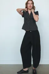 Camisa negra con estampado de lunares blancos, cuello redondo con escote en pico, mangas cortas abullonadas y detalle de volantes frontales. Cierre frontal con botones.