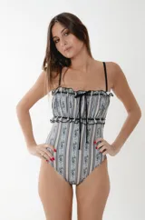 Traje de baño entero de lycra con estampado de rayas verticales y detalles florales sobre fondo celeste pálido. Presenta escote strapless fruncido con pasasinta negra, moño en el centro y breteles negros ajustables.