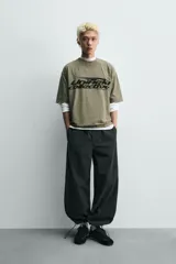 Camiseta de algodón con corte relajado, cuello redondo y manga corta. Presenta un estampado gráfico frontal en color negro con tipografía estilo deportivo y efecto desgastado.