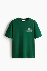 Remera verde de corte holgado en punto de algodón, con cuello redondo y diseño estampado en el pecho con texto y escudo que dice "The Hamptons Country Club".
