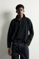 Polo relaxed fit de punto tejido en hilatura de algodón de color negro, con cuello solapa, cierre frontal de botonadura y manga larga.