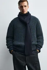 Jersey de punto grueso con estructura de volumen, corte relajado, cuello redondo y manga larga con puños y ruedo acanalados. Presenta un diseño bicolor con trama en tonos verde oscuro y azul.