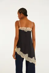 Blusa de breteles finos de color negro, con silueta amplia y caída asimétrica, confeccionada en tejido liviano con delicados detalles de encaje floral en el escote y el ruedo, y un gran aplique de encaje con diseño floral vertical en el frente.