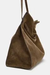Maxi bolso de hombro confeccionado en serraje, con diseño de silueta holgada y detalle de tira entrelazada en la parte frontal. Cuenta con asa de hombro, cierre mediante botón imantado y bolsillo interior con cremallera.