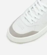 Championes urbanos blancos de material sintético con detalles en gris y negro. Presentan punta redonda, cordones, perforaciones para mayor respirabilidad y suela bold.