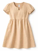 Vestido corto de broderie color beige, con escote en V, mangas cortas abullonadas y bolsillos laterales. Posee un corte a la cintura con falda de línea A.