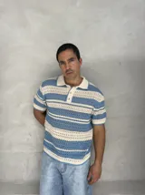 Remera tejida calada a rayas horizontales en celeste y crudo, con cuello polo y botones.