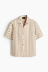 Camisa de manga corta con cuello abierto, confeccionada en una mezcla suave de lyocell. Presenta un diseño a rayas verticales, tapeta lisa, canesú en la espalda y bajo recto con aberturas laterales.