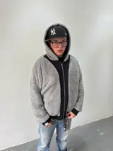 Campera reversible con cierre frontal, diseño oversize. Un lado es de algodón negro con estampados y bordados gráficos, mientras que el otro lado es de tela polar gris de pelo largo. Cuenta con capucha, puños y ruedo acanalados.