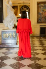 Vestido largo color rojo, de corte holgado con escote en V y mangas largas acampanadas. Presenta un detalle de volado horizontal en la cintura que aporta volumen y movimiento a la prenda.