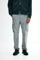 Pantalón cargo de nylon color gris claro, con cintura elástica y cordón ajustable. Presenta bolsillos laterales con cierre, bolsillos cargo con solapa en las piernas y cordón ajustable en los bajos.