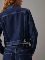 Campera de denim rígido color azul índigo oscuro, con corte cropped y ajuste auténtico de los 90. Presenta cuello en punta, bolsillos con solapa en el pecho y botones metálicos de la marca. Incluye una insignia con el logo de Calvin Klein en el bolsillo del pecho.
