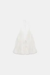 Top halter blanco de gasa con escote en V profundo, detalles de bordados a tono, tirantes finos para anudar al cuello y cierre frontal con cordones ajustables con lazadas.