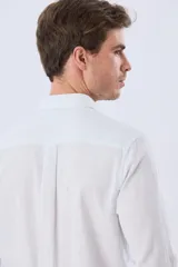 Camisa de lino a rayas finas en tonos beige y blanco, de manga larga con puños vueltos, cuello camisero y cierre frontal de botones. Cuenta con un pequeño logo bordado en el pecho.