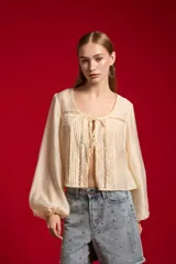Blusa de lyocell color natural, holgada y de manga larga, con cuello redondo, detalles de encaje y lazo para anudar en el frente.
