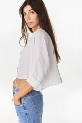 Camisa de lino azul marino, de corte crop y holgado, con cuello redondo, botonadura frontal y mangas amplias con vuelta.