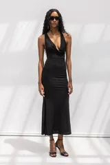 Vestido largo negro de corte al cuerpo, con escote halter y cuello drapeado. Presenta una silueta entallada que se ensancha suavemente hacia el ruedo.