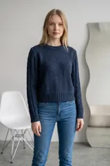 Sweater de punto color verde, con cuello redondo, diseño de trenzas en las mangas y detalle de relieve en el frente. Presenta un corte corto con puños y ruedo acanalados.