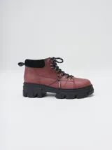 Bota acordonada de estilo montañés con suela track de goma robusta. Confeccionada en cuero con detalles de gamuza en la talonera y tirador trasero. Presenta costuras a contratono y cordones bicolores.