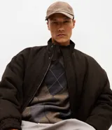 Campera bomber puffer de color marrón oscuro, confeccionada en poliéster con acabado texturizado. Presenta cuello alto, cierre frontal con cremallera, puños y ruedo elásticos.