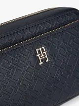 Cartera tipo bandolera Tommy Hilfiger con acabado granulado y diseño integral de monograma TH en relieve. Cuenta con cierre de cremallera, bolsillo exterior frontal con cierre, correa extraíble y apliques metálicos dorados, incluyendo la insignia del monograma TH en el frente.