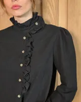 Camisa de manga larga con estampado de cuadros en tonos marrones y azules. Presenta cuello alto con volados, cierre frontal con botones y puños con volados.
