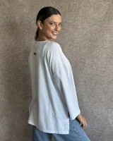 Remerón de algodón color crudo, con cuello redondo, mangas largas y bolsillo frontal. Presenta un diseño holgado con corte asimétrico, siendo más largo en la parte posterior.