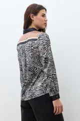 Camisa de manga larga con cuello camisero, estampado de cebra y detalles verticales en tonos negro, marrón y beige en el frente.