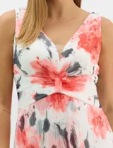 Vestido largo de chifón plisado con estampado floral en tonos rojos y grises sobre fondo blanco. Presenta escote en V pronunciado con panel de microtul, cintura drapeada con nudo central y falda amplia con capa frontal asimétrica. Incluye forro interior y cierre invisible en la espalda.