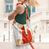 Bolso tipo tote bag de cuero vacuno color blanco con apliques de cuero naranja y dorado. Tiene cierre en la tapa trasera, interior forrado con bolsillo con cierre y bolsillo para el móvil. Incluye manija corta y correa larga ajustable y removible.
