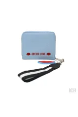 Billetera tipo monedero de cuero sintético negro con parche frontal blanco que incluye el texto 'MON AMOUR' y logo de la marca. Incluye una correa de muñeca a rayas y un dije colgante en forma de labios rojos.