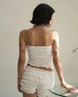 Top strapless blanco con detalle de frunces y moño negro en el centro.